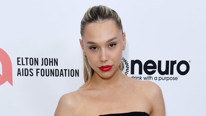 Alexis Ren poses in front of a white backdrop in a black strapless dress and red lipstick.